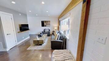 A modern living room with a sofa, coffee table, and a TV on a shelf.