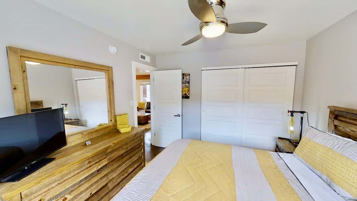 Een slaapkamer met een bed, een televisie op een houten dressoir, een plafondventilator en een kledingkast.