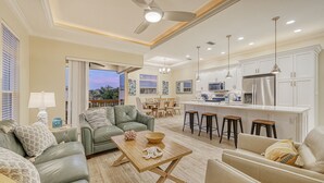 A spacious living area with a sofa, coffee table, and dining table. There is a kitchen with modern appliances and white cabinetry. - The Nautilus | Luxury Pet Friendly Home, 2 Heated Pools, Ping Pong Tables Steps to Beach! (Sarasota)
