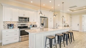 A modern kitchen with white cabinetry, stainless steel appliances, a large island with bar stools, and pendant lighting. - The Nautilus | Luxury Pet Friendly Home, 2 Heated Pools, Ping Pong Tables Steps to Beach! (Sarasota)
