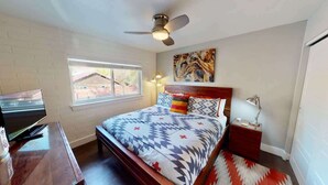 A bedroom with a bed, a ceiling fan, a window, a TV, and a nightstand. - Moab Flats - 5, Mid Century Modern on Main (Moab)