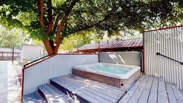 A hot tub with steps leading up to it, surrounded by a wooden deck and metal fencing.