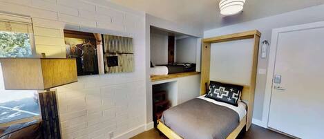 A bedroom with a bed, a built-in shelf, a wardrobe, and a window with a view.