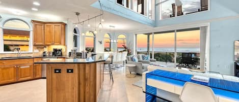 Una cocina amplia con armarios de madera, una isla central y un comedor con vista al océano.