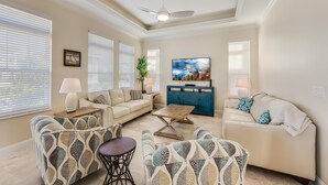 A living room with a beige sofa, patterned armchairs, a coffee table, and a TV on a blue cabinet.