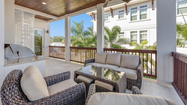 A covered patio area with wicker furniture, a ceiling fan, and a view of a white building with windows.