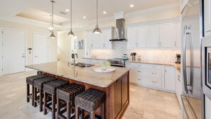 A spacious kitchen with a large island, white cabinetry, stainless steel appliances, and a modern pendant light fixture.