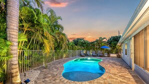A swimming pool with a curved edge, surrounded by a brick patio, palm trees, and a fence. - Casita Morning Star | Pet Friendly Home on Siesta Key, Heated Pool, Walk to Beach & South Village! (Siesta Key)