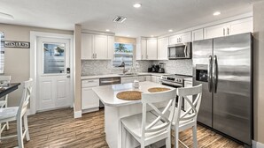 A modern kitchen with white cabinetry, stainless steel appliances, and a central island with two chairs. - Casita Morning Star | Pet Friendly Home on Siesta Key, Heated Pool, Walk to Beach & South Village! (Siesta Key)