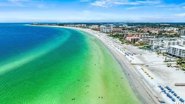 An aerial view of a beach with clear turquoise waters, a sandy shore, and a row of buildings with balconies overlooking the beach. - Casita Morning Star | Pet Friendly Home on Siesta Key, Heated Pool, Walk to Beach & South Village! (Siesta Key)