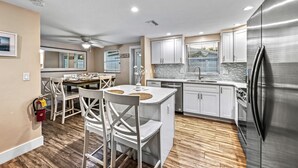 A modern kitchen with white cabinetry, a stainless steel refrigerator, and a dining area with white chairs and a small island. - Casita Morning Star | Pet Friendly Home on Siesta Key, Heated Pool, Walk to Beach & South Village! (Siesta Key)