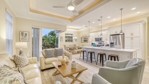 A spacious living area with a sofa, coffee table, and a dining table with chairs. There is a kitchen with modern appliances and a large island.