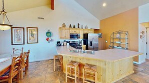 A kitchen with a central island, wooden chairs, a dining table, and a refrigerator. - Arches Abode - A3, 3 Bedroom Condo in Moab and Beautiful Views (Moab)