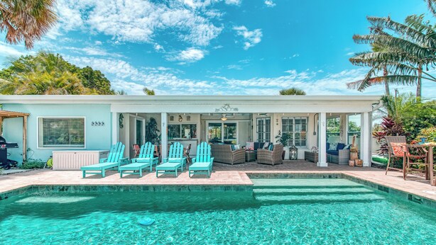 A poolside area with a clear pool, light blue Adirondack chairs, and a covered seating area with wicker furniture. - La Contento Casa | Pet Friendly, Waterfront Home on Siesta Key w/ Private Heated Pool & Kayaks! (Siesta Key)