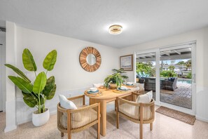 A dining area with a round wooden table, four wicker chairs, a large potted plant, and a wall-mounted mirror.