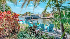 A patio area with turquoise chairs, a covered table, and a view of a body of water. - La Contento Casa | Pet Friendly, Waterfront Home on Siesta Key w/ Private Heated Pool & Kayaks! (Siesta Key)