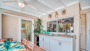 A kitchen with white cabinets, a granite countertop, and a backsplash. There is a dining table with chairs and a ceiling fan. - La Contento Casa | Pet Friendly, Waterfront Home on Siesta Key w/ Private Heated Pool & Kayaks! (Siesta Key)