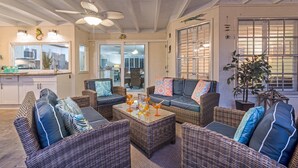 A cozy living area with wicker furniture, a ceiling fan, and a view of the kitchen through glass doors. - La Contento Casa | Pet Friendly, Waterfront Home on Siesta Key w/ Private Heated Pool & Kayaks! (Siesta Key)