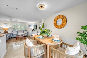 A modern living room with a dining area, featuring a round wooden table, wicker chairs, and a large mirror on the wall.