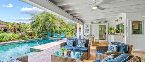 A covered outdoor area with a pool, wicker furniture, and a dining area.