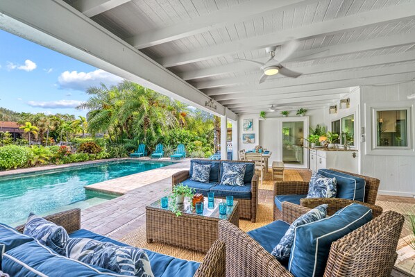 A covered outdoor area with a pool, wicker furniture, and a dining area.