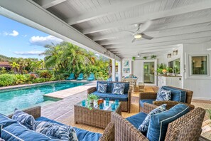 A covered outdoor area with a pool, wicker furniture, and a dining area.