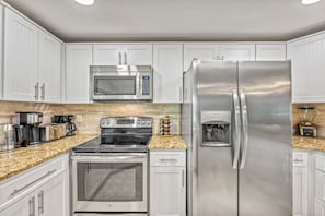Una cocina moderna con electrodomésticos de acero inoxidable, armarios blancos y encimeras de granito.