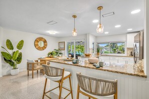 A modern kitchen with a central island, pendant lighting, and a view to the outside.