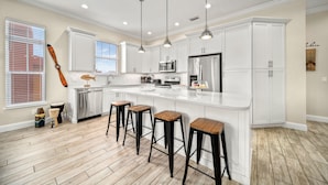 A modern kitchen with white cabinets, a stainless steel refrigerator, a microwave, and a large island with bar stools. - Casa Mahalo | Pet Friendly, Ping Pong Table, Private Heated Pool, Steps to Beach! (Siesta Key)