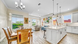 A spacious kitchen with white cabinetry, a wooden dining table, and a large island. - Casa Mahalo | Pet Friendly, Ping Pong Table, Private Heated Pool, Steps to Beach! (Siesta Key)