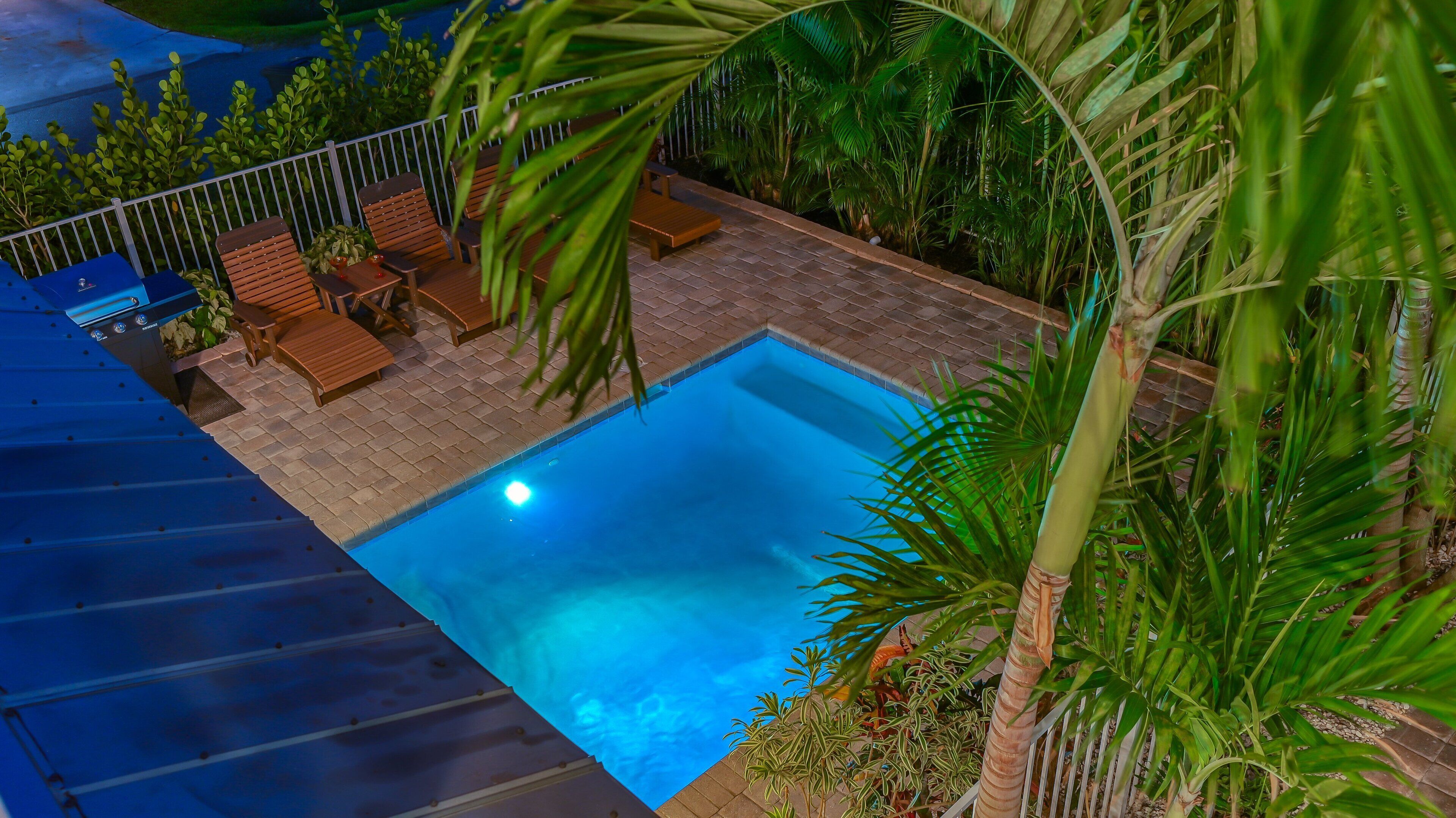 Una piscina exterior amb solàrium de rajola, envoltada de vegetació exuberanta i gandules de fusta.