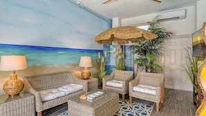 A room with a beach mural, wicker furniture, a thatched umbrella, and a large potted plant. - 🦋 Casa De Mariposa | Heated Pool, Gulf Views, Dual-Villa Duplex, Walk to Siesta Key Beach (Siesta Key)