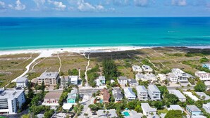 An aerial view of a coastal residential area with houses, a beach, and a clear blue sky.