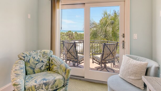 A room with a sliding glass door leading to a balcony with outdoor furniture and a view of the ocean.
