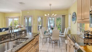 A kitchen with granite countertops, stainless steel appliances, and a dining area with white chairs and a glass table.