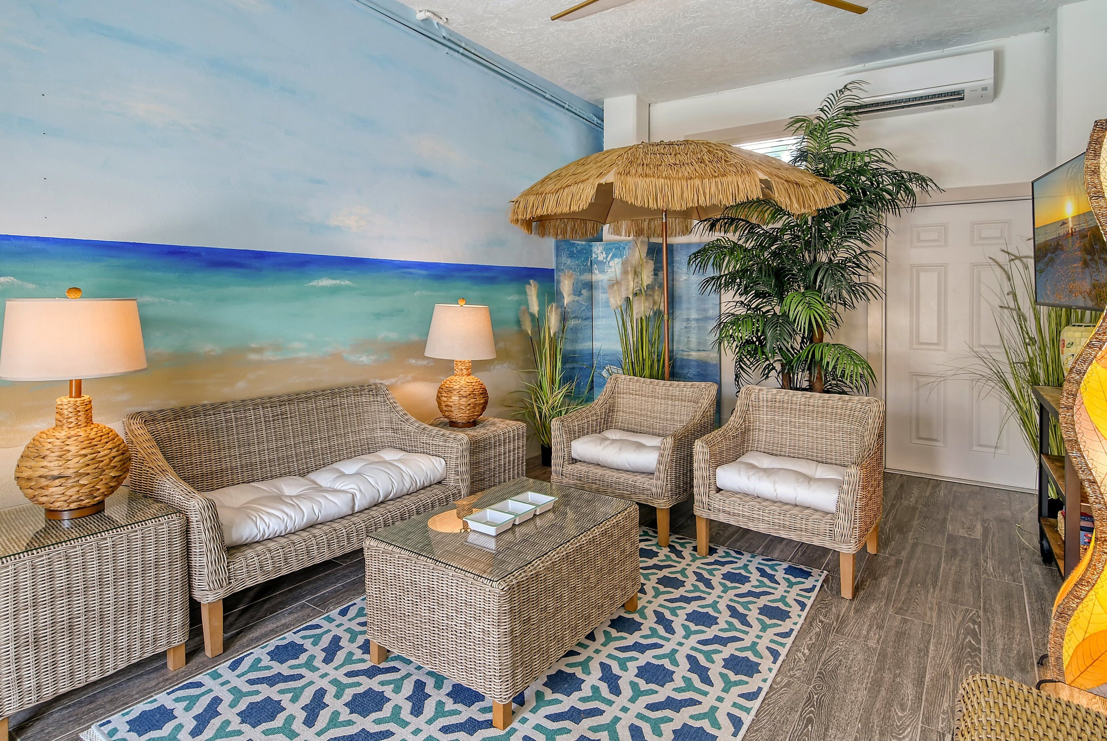 A beach-themed living area with wicker furniture, a large painting of a beach, and a tropical plant.