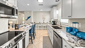 A modern kitchen with stainless steel appliances, a granite countertop, and a central island with bar stools. - Sandy Cabana | Pet Friendly Home on Siesta Key w/ Heated Pool, Short Walk to Beach! (Siesta Key)