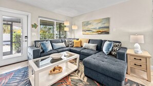 A modern living room with a sectional sofa, a glass coffee table, and a side table with a lamp. - Sandy Cabana | Pet Friendly Home on Siesta Key w/ Heated Pool, Short Walk to Beach! (Siesta Key)
