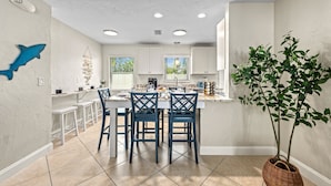 A modern kitchen with white cabinets, a dining area with blue chairs, and a large potted plant. - Sandy Cabana | Pet Friendly Home on Siesta Key w/ Heated Pool, Short Walk to Beach! (Siesta Key)