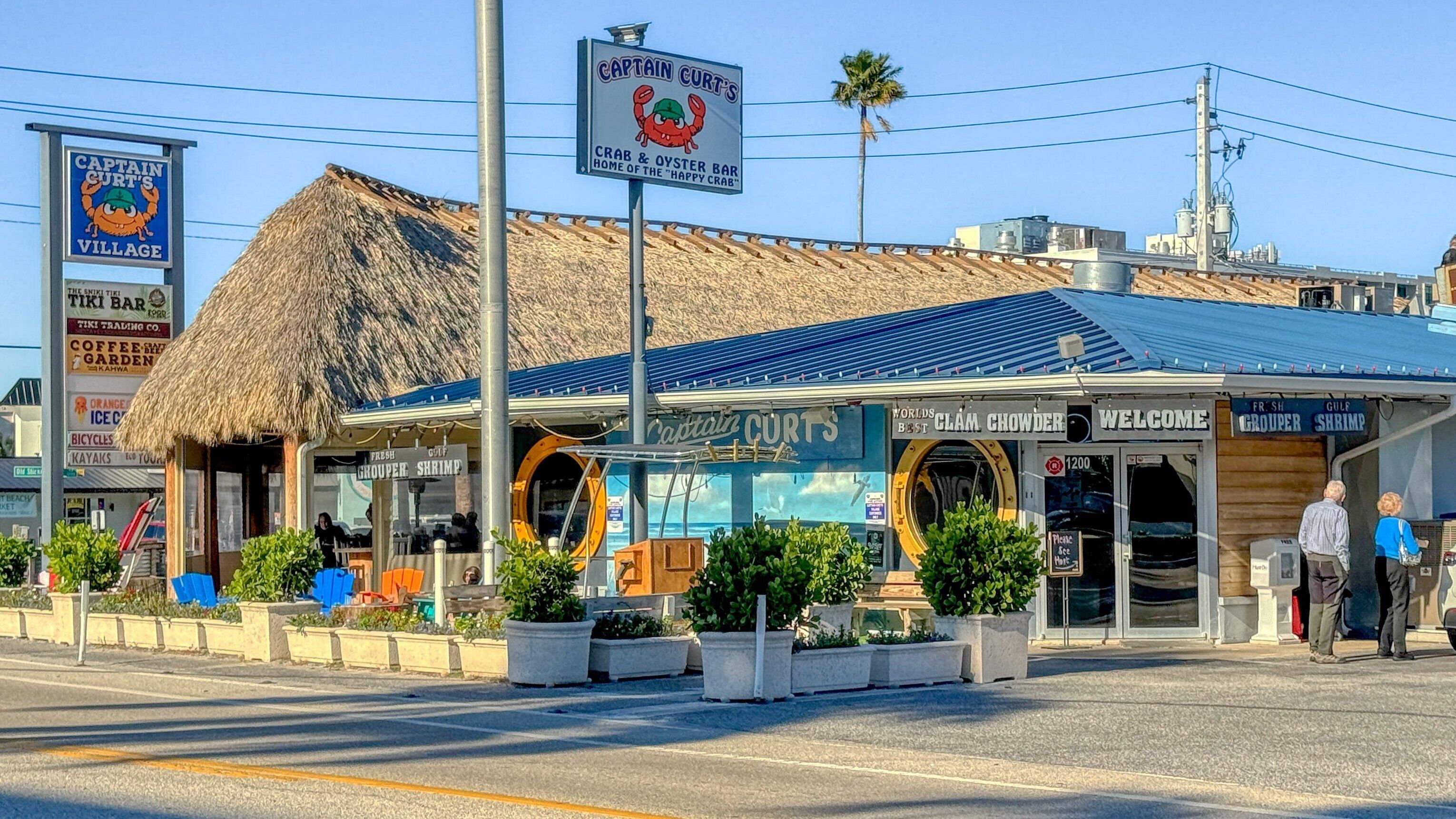 A coastal bar named Captain Curt's Village with a thatched roof and a sign featuring a crab mascot.