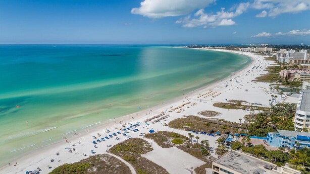 A beach resort with a wide sandy beach, clear turquoise waters, and a few buildings in the background. - Sandy Cabana | Pet Friendly Home on Siesta Key w/ Heated Pool, Short Walk to Beach! (Siesta Key)