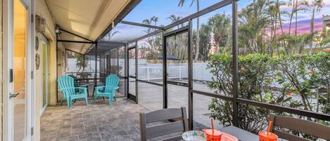 A covered outdoor seating area with tables and chairs, a view of palm trees, and a patio door.