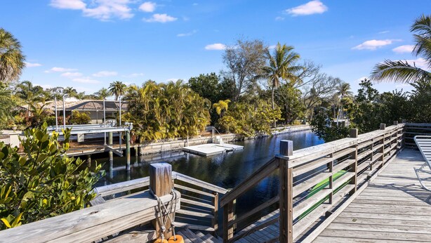 A wooden dock extending over a calm water body, surrounded by lush greenery and palm trees. - Villa De Paradisio | Waterfront Home w/ Private Pool, Fishing Dock, Close to Beach & Village! (Siesta Key)