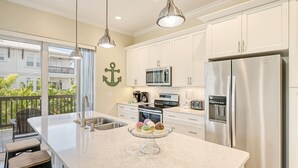 A modern kitchen with stainless steel appliances, a large island with a glass top, and a view of the balcony.