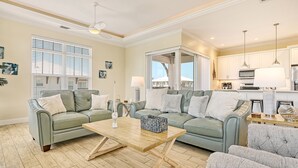 A spacious living room with two green sofas, a wooden coffee table, and a view of the kitchen.