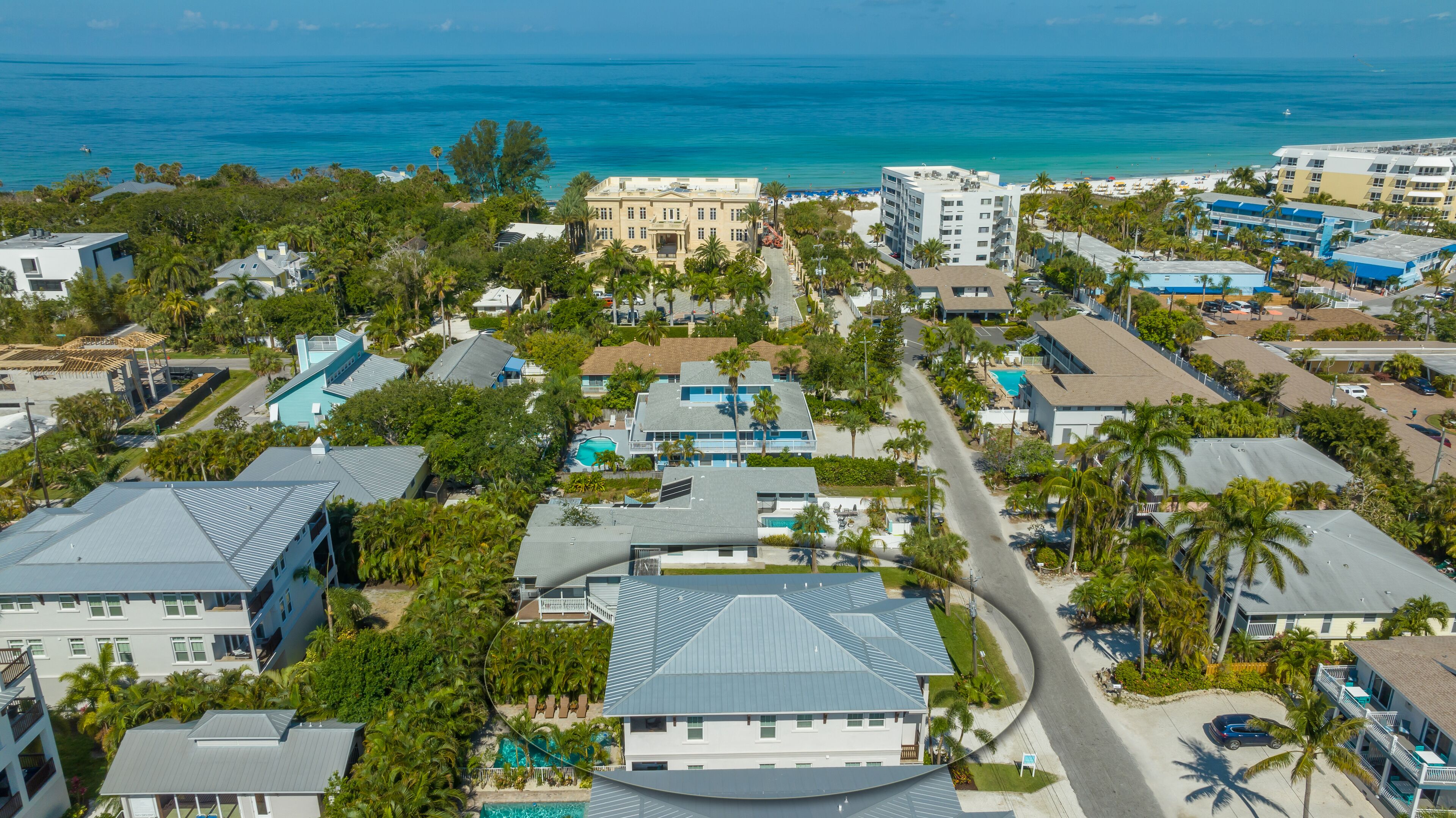 Vue aérienne d’un quartier résidentiel situé sur la côte, avec de nombreux bâtiments, dont une grande maison dotée d’une piscine et un bâtiment plus petit avec un toit bleu.
