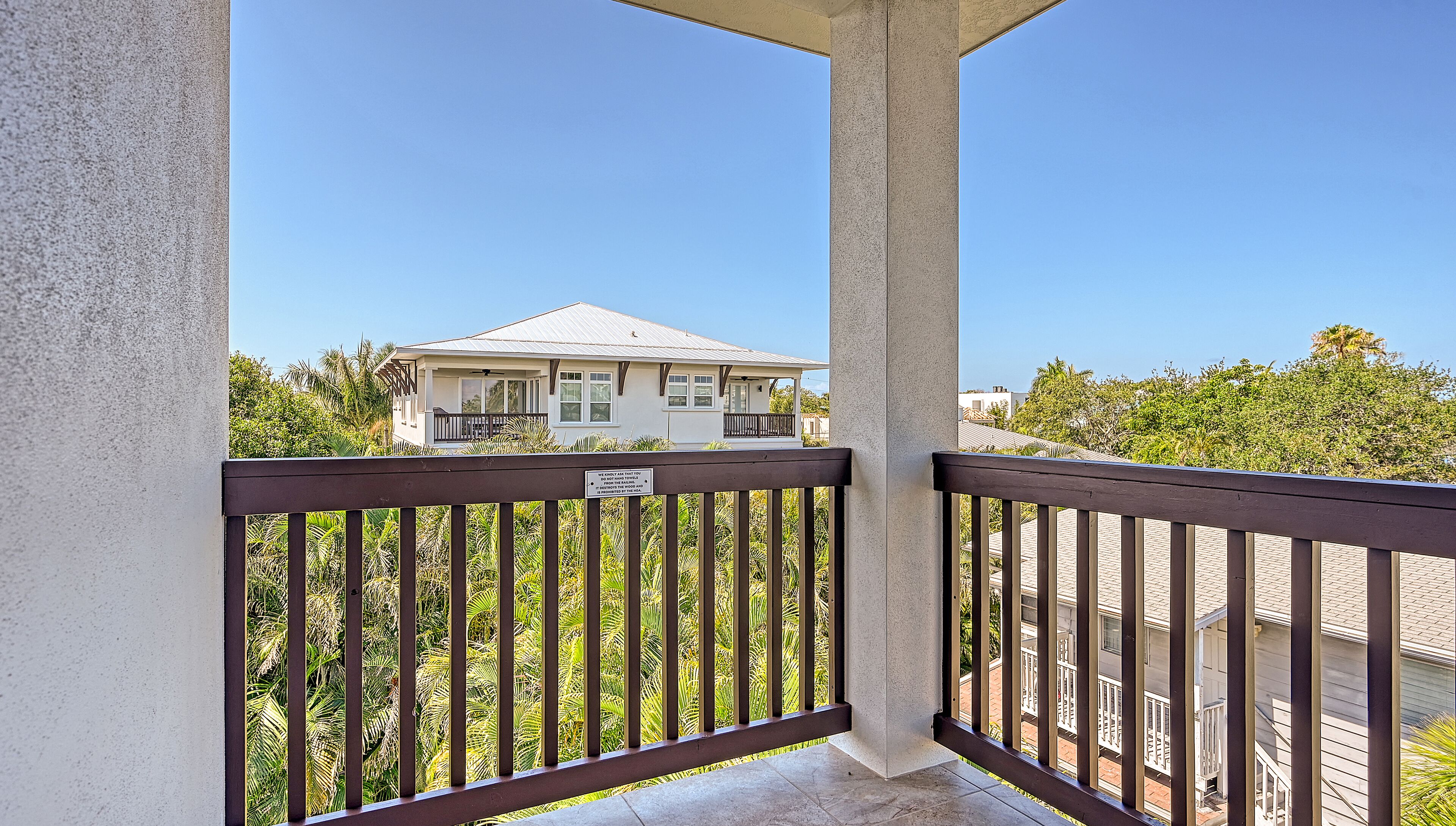 A balcony with a view of a house and surrounding greenery.