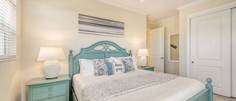 A bedroom with a teal-colored bed, two bedside tables with lamps, a patterned rug, and a door with a mirror.