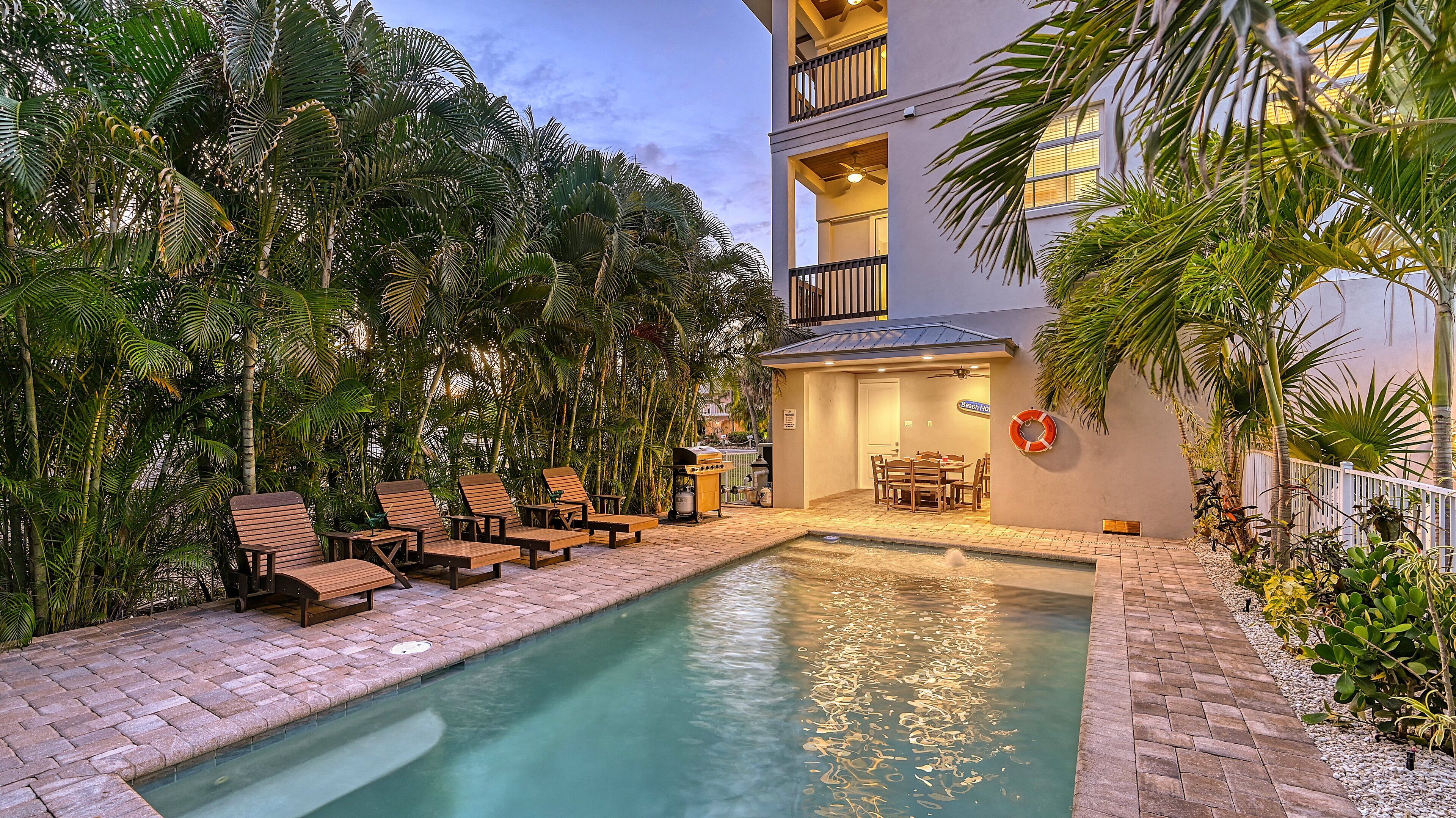 Un espace piscine doté de chaises longues et d’un barbecue, le tout entouré d’une végétation tropicale luxuriante.