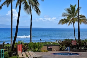 A pool area with lounge chairs and a view of the ocean.